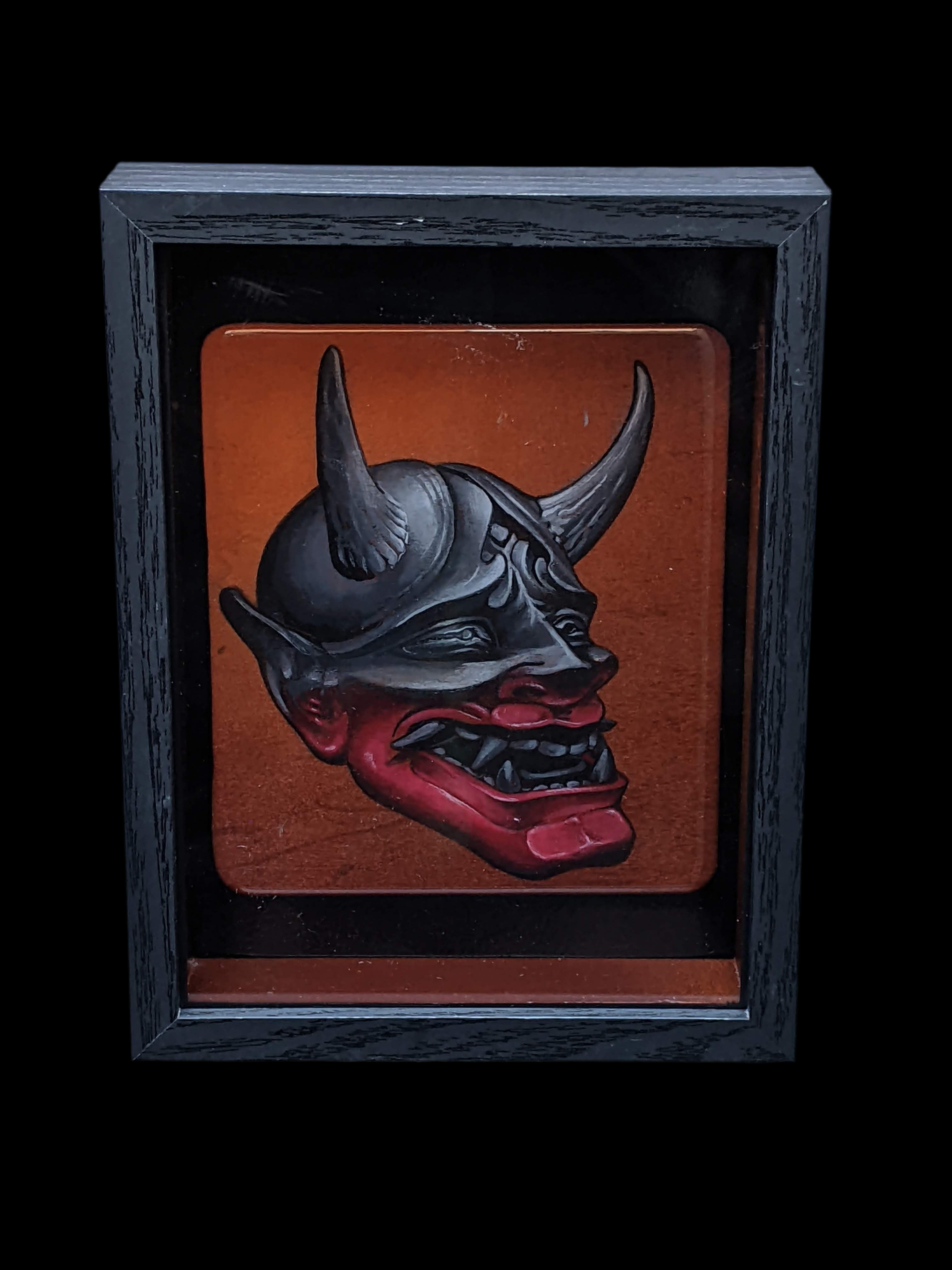 Resin art plaque with a horned mask design in a black frame on a black background